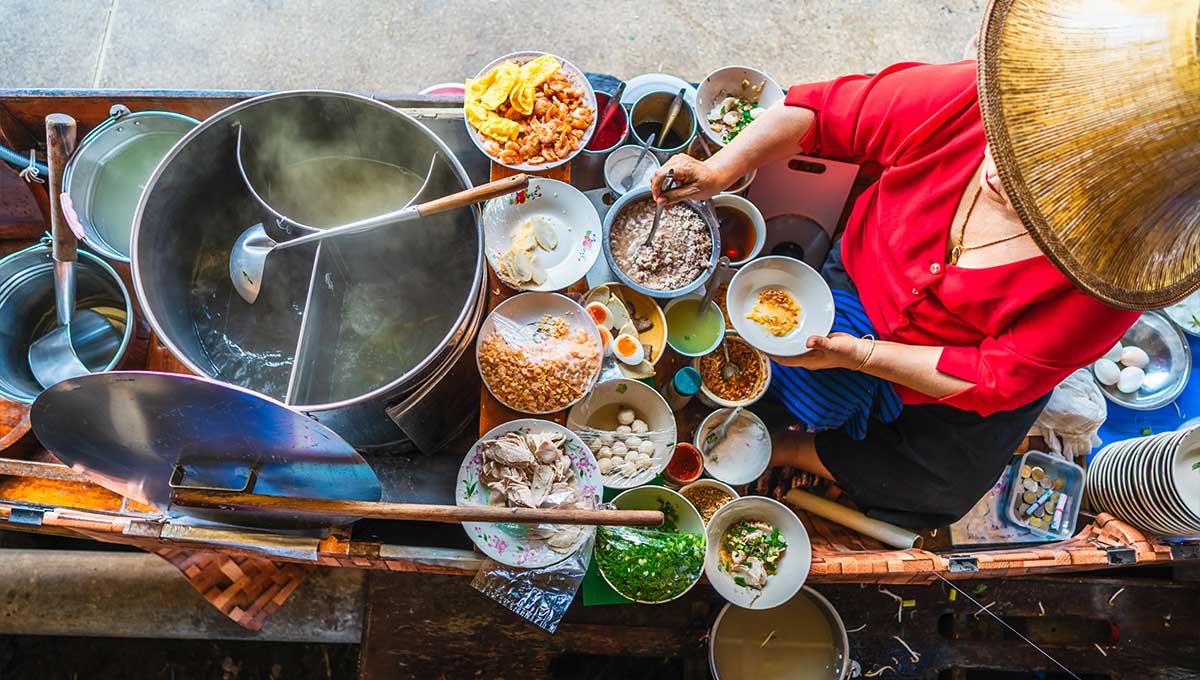Top view old woman cooking Thai noodle soup Tom Yam style on Thai tradition boat in local floating market Famous traditional Thai street food for tourist people travel Bangkok Thailand